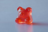 Single red translucent gummy bear candy on a light gray background, casting a soft shadow, close-up macro shot for food and confectionery use.
