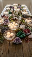 Floating candles in glass bowls surrounded by healing crystals, moss and dried botanicals create peaceful spa meditation atmosphere on rustic wooden surface.