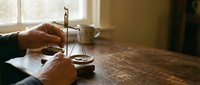 Traditional brass balance scale in hands on wooden table with warm natural lighting for justice and legal concepts.