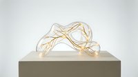 Elegant glass sculpture with glowing golden branches inside, displayed on a pedestal against a neutral background, blending art and light design.