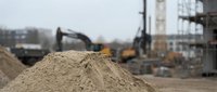 Pile of construction sand at building site with excavator and crane equipment in background for infrastructure development projects.