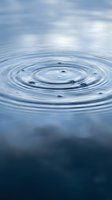Water ripples creating concentric circles on calm blue surface with cloudy sky reflection, symbolizing tranquility, meditation and peaceful nature concepts.