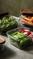 Meal prep containers with fresh vegetables including snap peas, radishes, carrots and mixed greens for healthy eating and food storage.