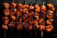 Grilled chicken yakitori skewers with sweet and savory glaze on dark background, close up view showing caramelized char marks and glossy sauce coating.