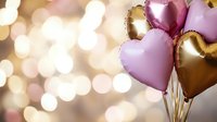 Heart-shaped pink and gold foil balloons against blurred bokeh lights background, romantic celebration atmosphere for Valentine's day or anniversary party.
