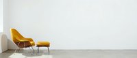 Modern mustard yellow armchair with matching ottoman and metal legs positioned against white wall in minimalist interior space for contemporary home decor and furniture design projects.