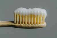 Bamboo toothbrush with white toothpaste foam on bristles against neutral gray background, showcasing eco-friendly dental care.