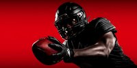 American football player in black uniform holding ball against dramatic red background, showcasing strength and determination in sports action pose.
