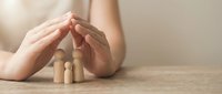 Protective hands covering wooden family figures on table representing insurance, safety, care and family protection concept for financial security planning.