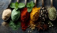 Colorful spices and herbs in vintage metal spoons on dark slate background, aromatic cooking ingredients for culinary use.