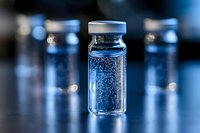 Medical vial with blue liquid and bubbles on dark background with bokeh effect, selective focus on center bottle, multiple vials in soft blur background.