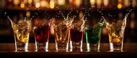 Row of colorful cocktails with dynamic splashes on wooden bar counter against warm bokeh lights background for party celebrations.