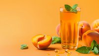 Fresh peach juice in tall glass with mint garnish on orange background, healthy summer drink with sliced fruit for refreshing beverage concepts.