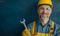 Mature Caucasian maintenance worker in yellow hard hat and overalls holding wrench, wearing safety glasses and smiling confidently against dark background.