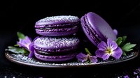 Purple macarons dusted with powdered sugar on dark plate with violet flower garnish against black background, dramatic food photography styling.
