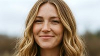 Smiling young Caucasian woman with freckles and wavy blonde hair outdoors, close-up portrait with natural background and warm expression.