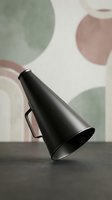 Modern black metal megaphone on dark surface with abstract geometric shapes background in muted earth tones for communication and announcement concepts.