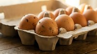 Fresh brown eggs in cardboard carton on rustic wooden table with warm natural lighting for organic farm produce and healthy cooking concepts.
