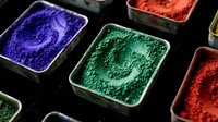 Assorted vibrant pigment powders in containers including blue, green, and red shades for art, cosmetics, and craft projects.