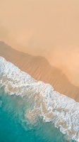 Aerial view of pristine turquoise ocean waves meeting golden sandy beach shore with white foam creating natural patterns on tropical coastline.