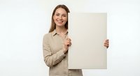 Smiling young Caucasian businesswoman in beige blazer holding blank white poster board for marketing presentations and promotional campaigns.