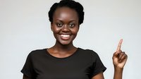 Young African American woman in black t-shirt pointing up with finger, smiling at camera on light background for advertising and promotional content.