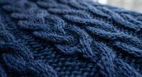 Navy blue cable knit wool sweater texture with intricate braided pattern detail for cozy winter fashion and textile design projects.