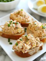 Tuna salad sandwiches on toasted bread with chopped eggs and fresh chives served on white plate for healthy lunch meal preparation and appetizer recipes.