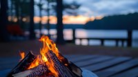 Cozy campfire burning brightly at lakeside dock during golden sunset hour, creating warm atmosphere for outdoor recreation and relaxation by water.