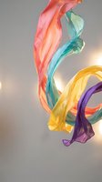 Colorful flowing fabric ribbons in motion creating dynamic waves with coral pink turquoise yellow and purple silk materials dancing in air against soft background.