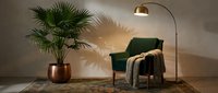 Cozy reading nook with green armchair, arc floor lamp, potted palm plant, and knit throw blanket on neutral rug. Interior design and home decor.