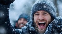 Joyful Caucasian man laughing during snowfall wearing winter hat and jacket, with friend in background. Natural outdoor portrait capturing genuine happiness in cold weather.