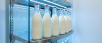 Fresh milk bottles lined up in modern refrigerated display case with blue LED lighting for dairy product storage and retail presentation.