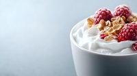 Fresh raspberries and crunchy walnuts top creamy yogurt or whipped dessert in white ceramic bowl against light blue background, selective focus.