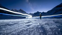 Solitary figure standing on frozen lake at night with light trails crossing snowy landscape and mountain peaks under starry sky, conveying isolation and winter adventure.