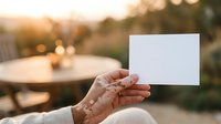 Mature woman holding blank white card outdoors at sunset with garden furniture and blurred background, suitable for advertising, marketing campaigns, and promotional materials.