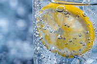 Fresh lemon slice in sparkling water with bubbles against blue background, macro photography showing crystal clear droplets and citrus detail.