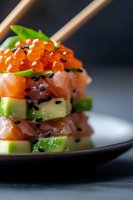 Fresh salmon tartare layered with diced avocado, topped with red caviar and black sesame seeds, served on dark plate with chopsticks, macro food photography.