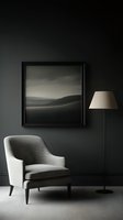 Minimalist interior with gray upholstered armchair against dark wall, black-framed landscape artwork, and floor lamp with beige shade creating moody atmosphere.