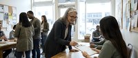 Professional blonde businesswoman mentor coaching young Asian female employee at modern office desk during team meeting and workplace collaboration.
