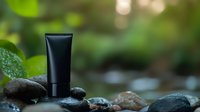 Black cosmetic tube on spa stones with water drops against blurred green natural background, wellness and beauty product photography.