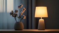 Minimalist home decor with table lamp casting warm light and cotton stems in ceramic vase against moody dark background, creating cozy atmosphere.