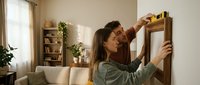 Young couple using level tool hanging picture frame on living room wall during home renovation and interior decorating project together.