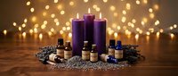 Purple candles with essential oil bottles and lavender flowers on wooden table with warm bokeh lights creating relaxing spa atmosphere for aromatherapy wellness.