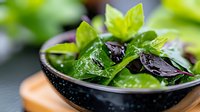 Fresh mixed salad greens with purple basil leaves in black ceramic bowl, water droplets on leaves, close-up view showing texture and vibrant colors.