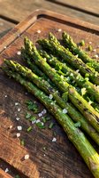 Grilled asparagus spears with sea salt and fresh herbs on wooden cutting board, ready for cooking or serving as a healthy vegetable side dish.