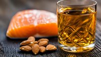 Fresh raw salmon fillet with scattered almonds and crystal glass of whiskey on dark wooden background, luxury food and drink pairing concept.