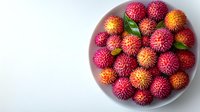 Fresh ripe rambutan fruits with bright pink and orange spiky skin arranged in gray ceramic bowl on white background, top view composition.