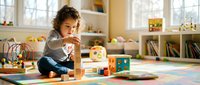 Young mixed-race toddler girl playing with colorful wooden blocks and educational toys on playroom floor. Child development and early learning concept.