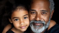Close up portrait of African American grandfather with gray beard and mixed race granddaughter smiling together, showing family bond and generational connection.